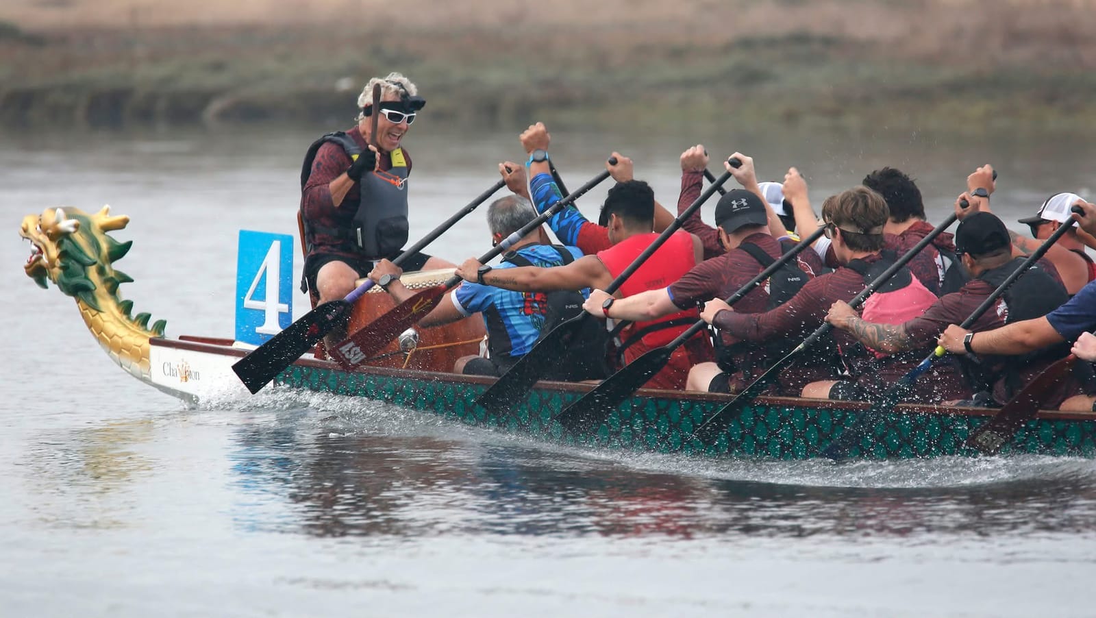 The crew in maroon drives the boat forward, dragon head leading, as the drummer raises a fist.
